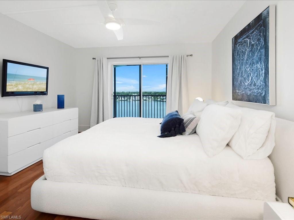 Bedroom featuring access to exterior, dark wood-style floors, a water view, and a ceiling fan