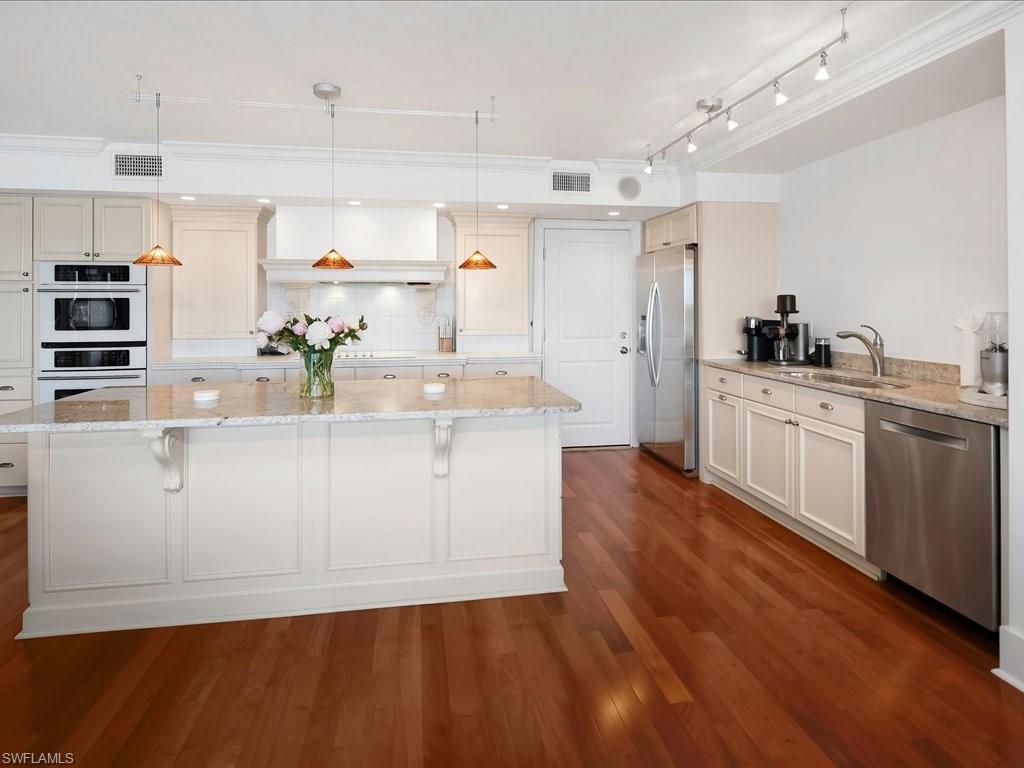 Kitchen featuring decorative light fixtures, light stone counters, stainless steel appliances, tasteful backsplash, and a center island