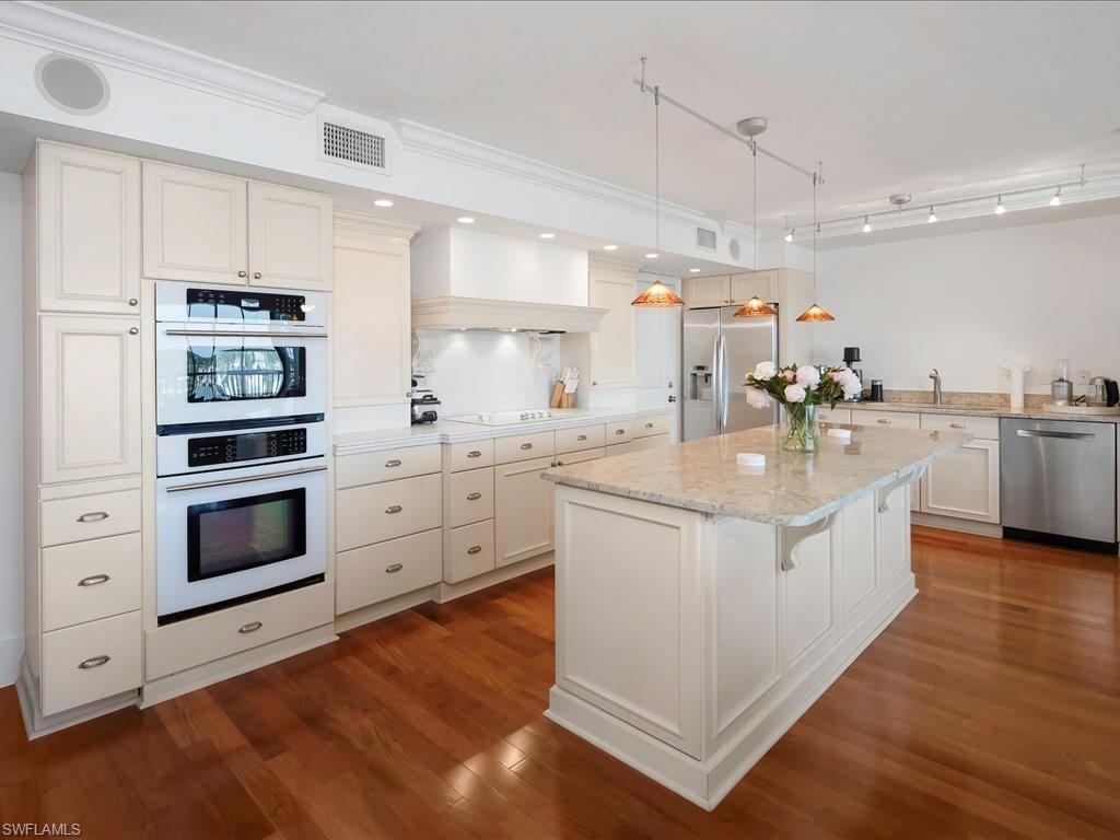Kitchen with pendant lighting, stainless steel appliances, dark wood-type flooring, light stone counters, and a kitchen bar