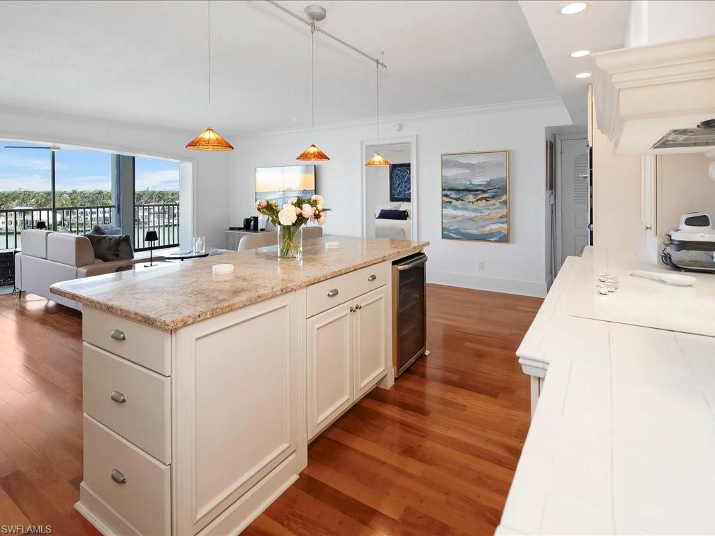 Kitchen featuring dark wood-style flooring, hanging light fixtures, beverage cooler, light stone countertops, and recessed lighting