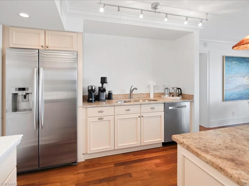 Kitchen featuring appliances with stainless steel finishes, light wood-style floors, light stone counters, ornamental molding, and recessed lighting