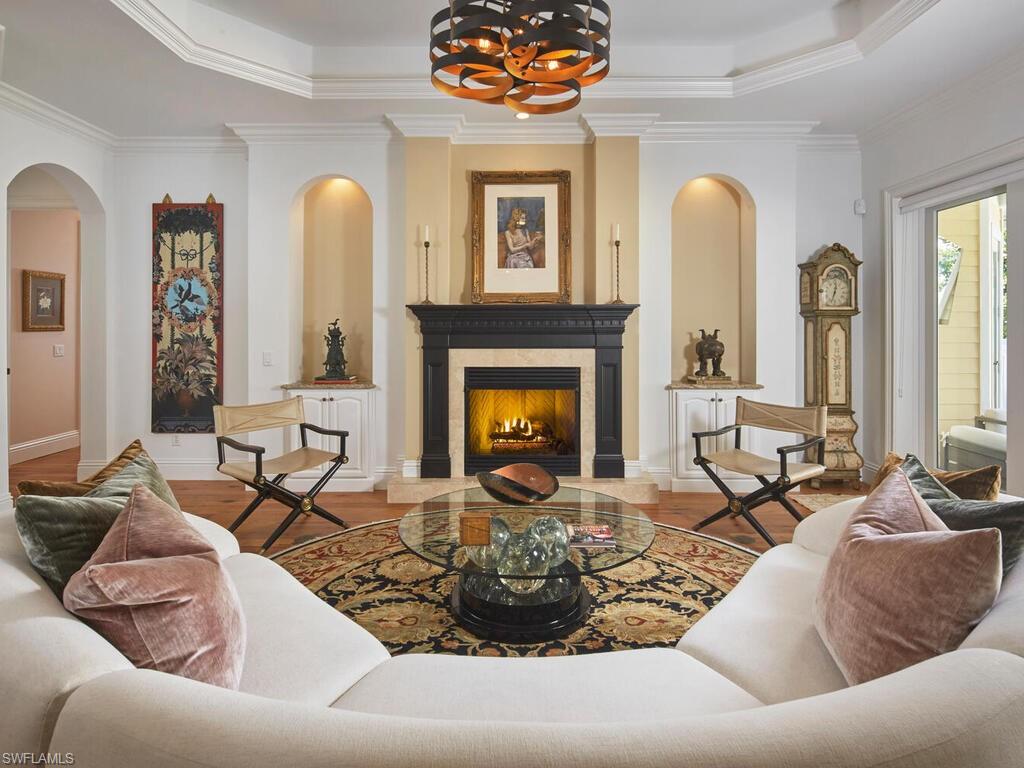 Living area featuring crown molding, a premium fireplace, arched walkways, a tray ceiling, and wood finished floors