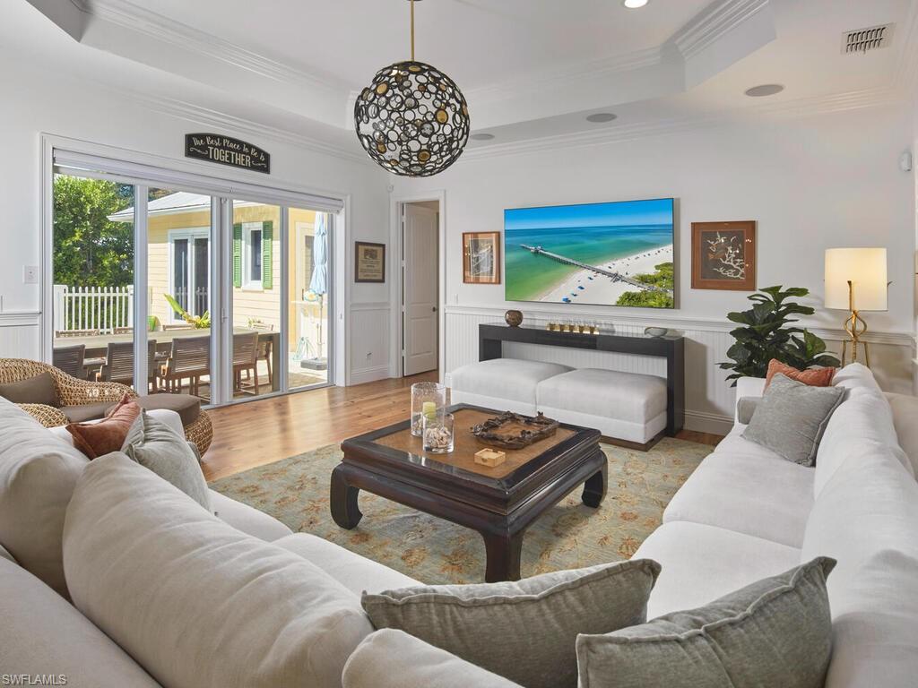 Living area with crown molding, healthy amount of natural light, wood finished floors, a raised ceiling, and a wainscoted wall