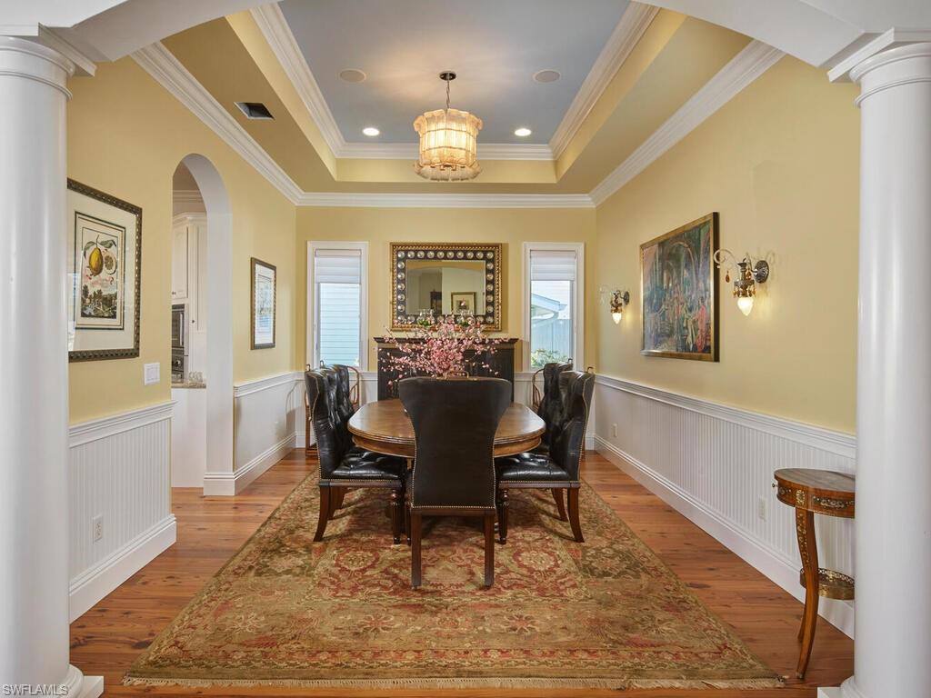 Dining room featuring ornate columns, arched walkways, light wood finished floors, crown molding, and a wainscoted wall