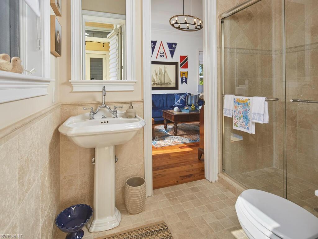 Bathroom featuring a wainscoted wall, a stall shower, tile walls, a chandelier, and crown molding