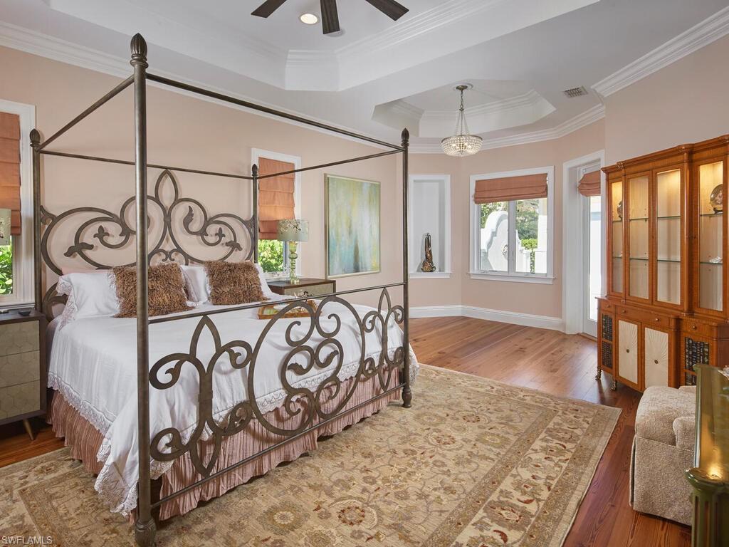 Bedroom featuring ornamental molding, a raised ceiling, hardwood / wood-style flooring, and ceiling fan