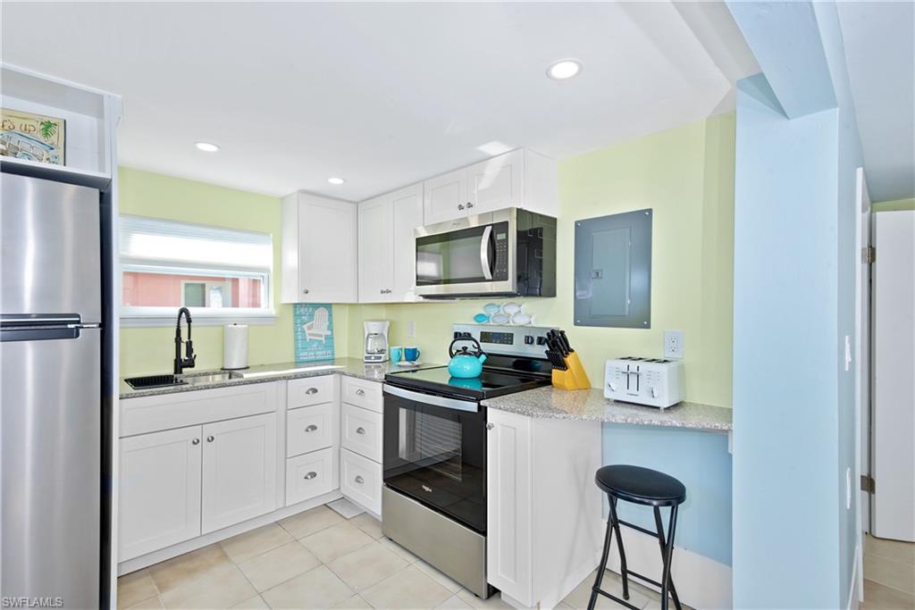 Kitchen featuring stainless steel appliances, light stone countertops, white cabinetry, electric panel, and light tile patterned floors - Virtually Edited Image