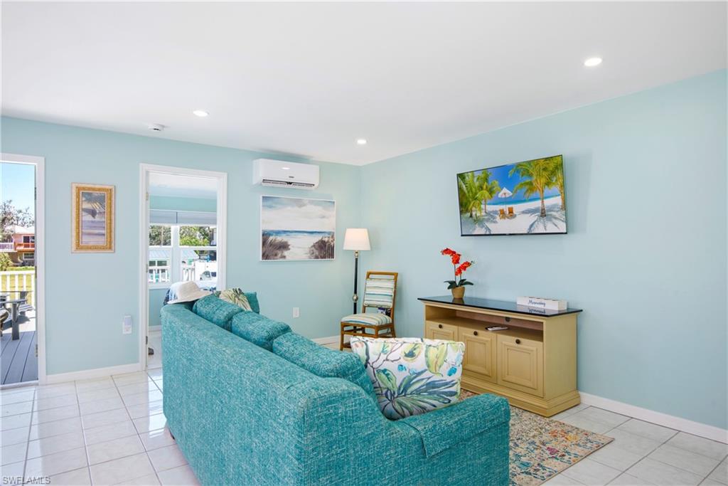 Living room with light tile patterned floors, recessed lighting, and a wall mounted air conditioner - Virtually Edited Image