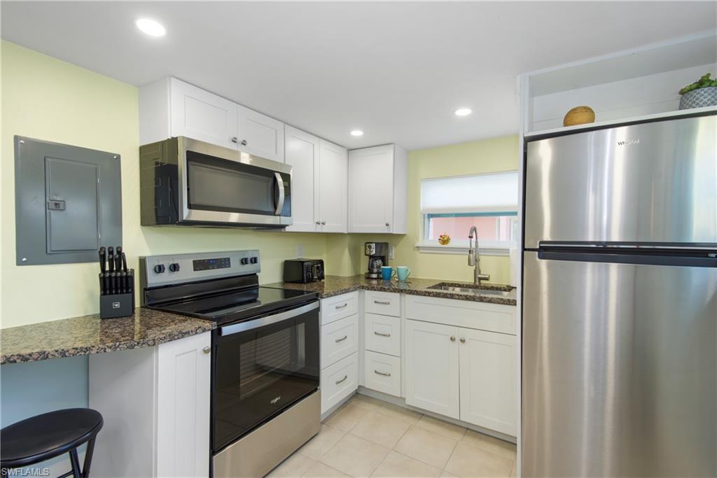 Kitchen featuring appliances with stainless steel finishes, electric panel, white cabinets, light tile patterned flooring, and recessed lighting - Virtually Edited Image