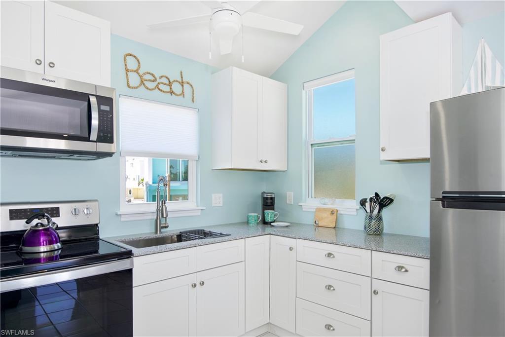 Kitchen featuring stainless steel appliances, plenty of natural light, white cabinetry, and lofted ceiling - Virtually Edited Image