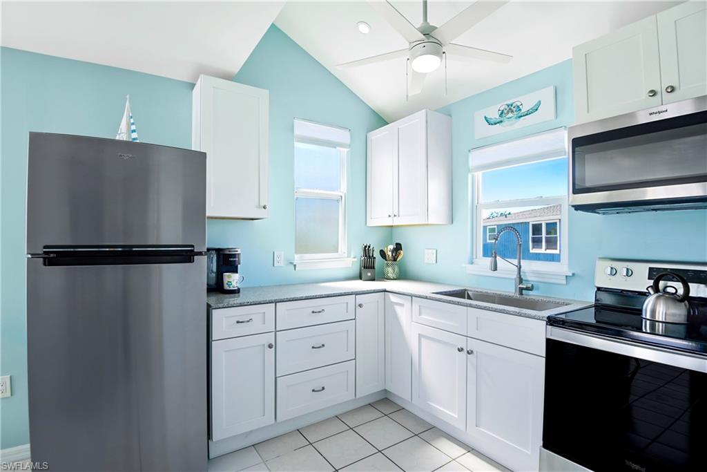 Kitchen featuring stainless steel appliances, white cabinetry, light tile patterned floors, a ceiling fan, and vaulted ceiling - Virtually Edited Image