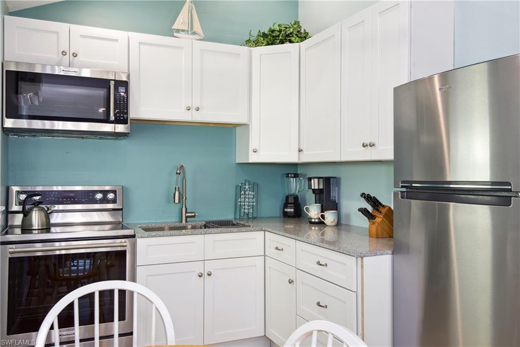 Kitchen with white cabinetry, appliances with stainless steel finishes, and light stone countertops - Virtually Edited Image