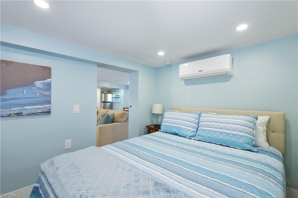 Bedroom featuring a wall mounted air conditioner, recessed lighting, and freestanding refrigerator - Virtually Edited Image