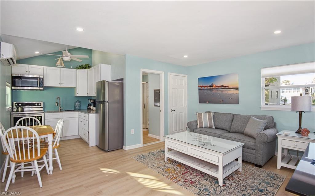 Living area with light wood-style floors, a wall unit AC, recessed lighting, and a ceiling fan - Virtually Edited Image