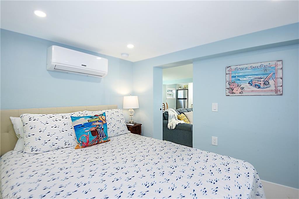 Bedroom with an AC wall unit, recessed lighting, and freestanding refrigerator - Virtually Edited Image