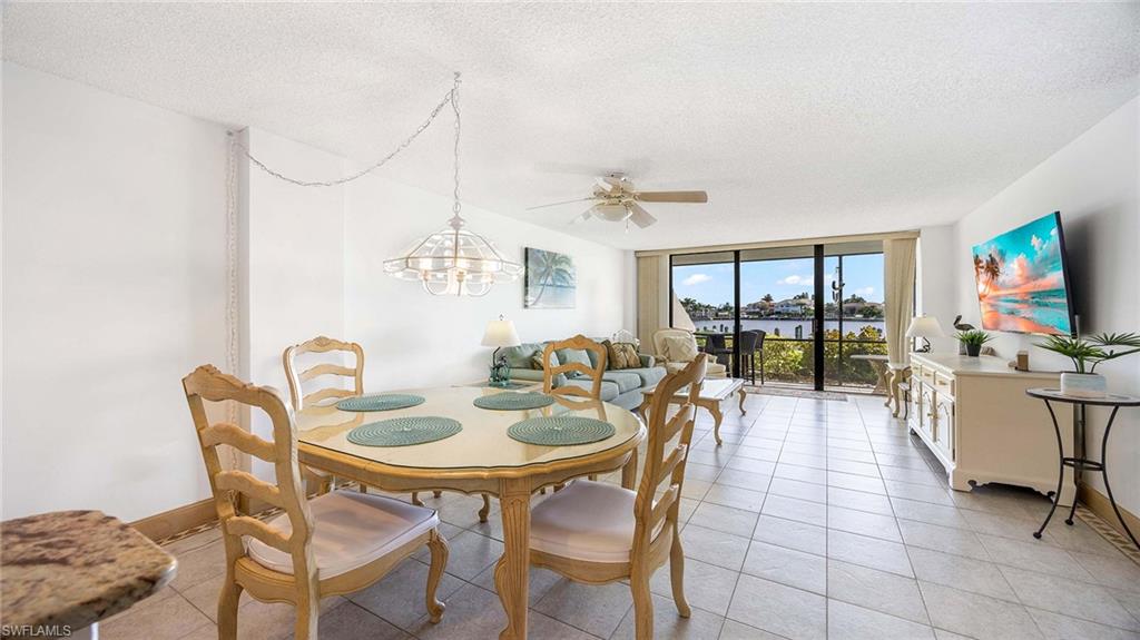 Dining space featuring floor to ceiling windows, a textured ceiling, a ceiling fan, light tile patterned flooring, and a chandelier
