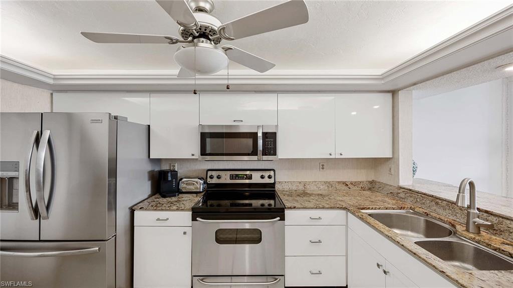 Kitchen with stainless steel appliances, light stone counters, white cabinets, and a ceiling fan