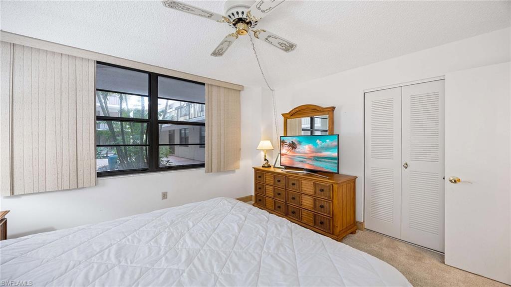 Bedroom with light colored carpet, a textured ceiling, a ceiling fan, and a closet