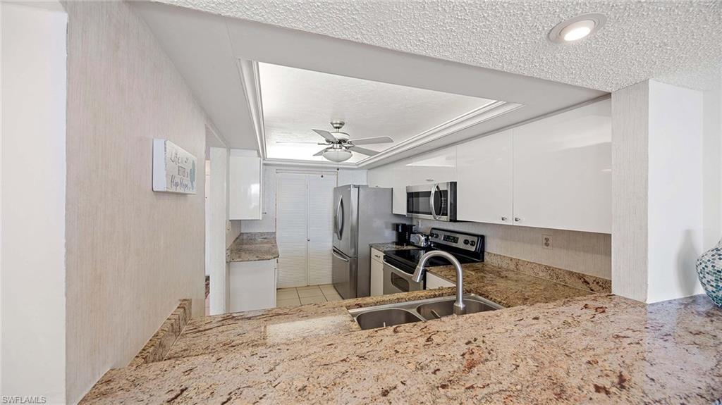 Kitchen featuring white cabinets, appliances with stainless steel finishes, light stone counters, a textured ceiling, and ceiling fan