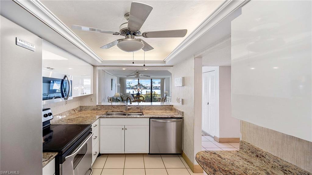 Kitchen with stainless steel appliances, light stone countertops, a raised ceiling, light tile patterned floors, and ornamental molding