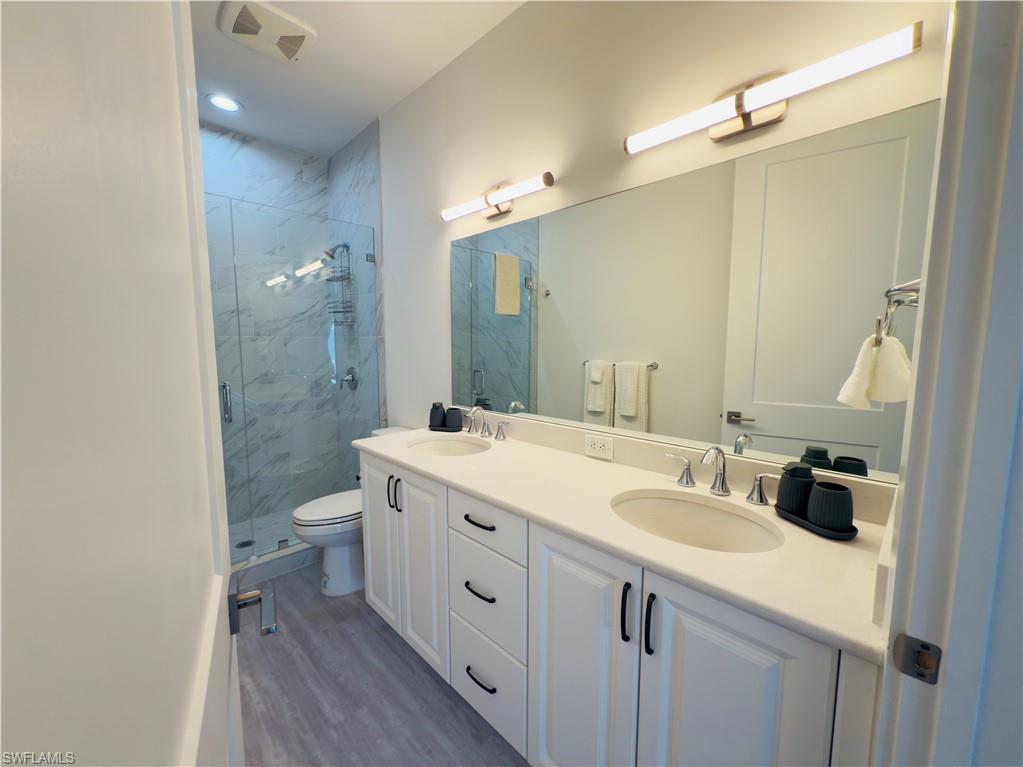 Bathroom featuring double vanity, a marble finish shower, and dark wood-style flooring