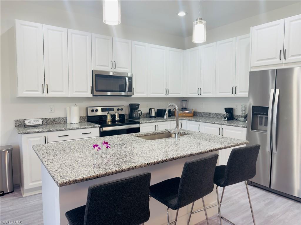 Kitchen with appliances with stainless steel finishes, decorative light fixtures, light stone countertops, white cabinets, and a breakfast bar