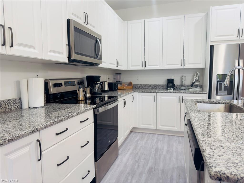 Kitchen with appliances with stainless steel finishes, white cabinetry, light stone countertops, and light wood-style flooring