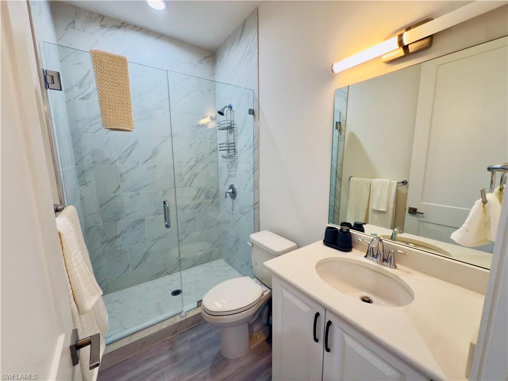 Bathroom featuring vanity, a marble finish shower, and dark wood finished floors