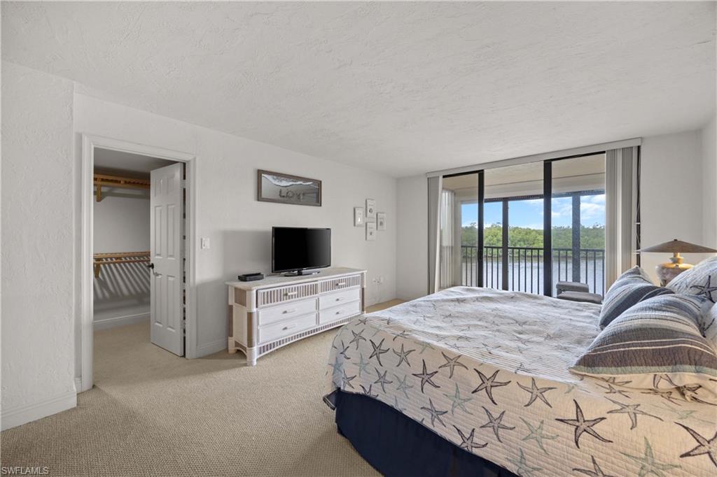 Bedroom featuring access to outside, a walk in closet, light carpet, and a textured ceiling