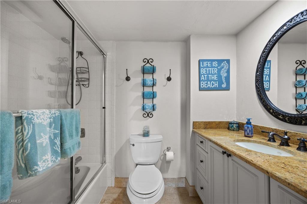 Full bathroom with tile patterned flooring, vanity, enclosed tub / shower combo, and toilet