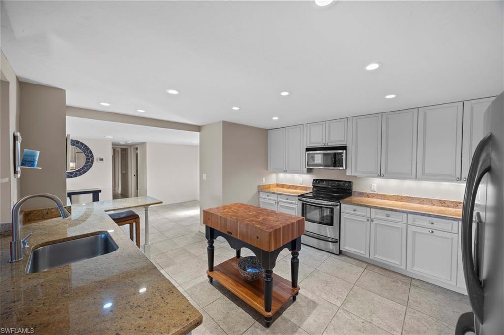 Kitchen featuring light stone countertops, sink, light tile patterned flooring, and appliances with stainless steel finishes