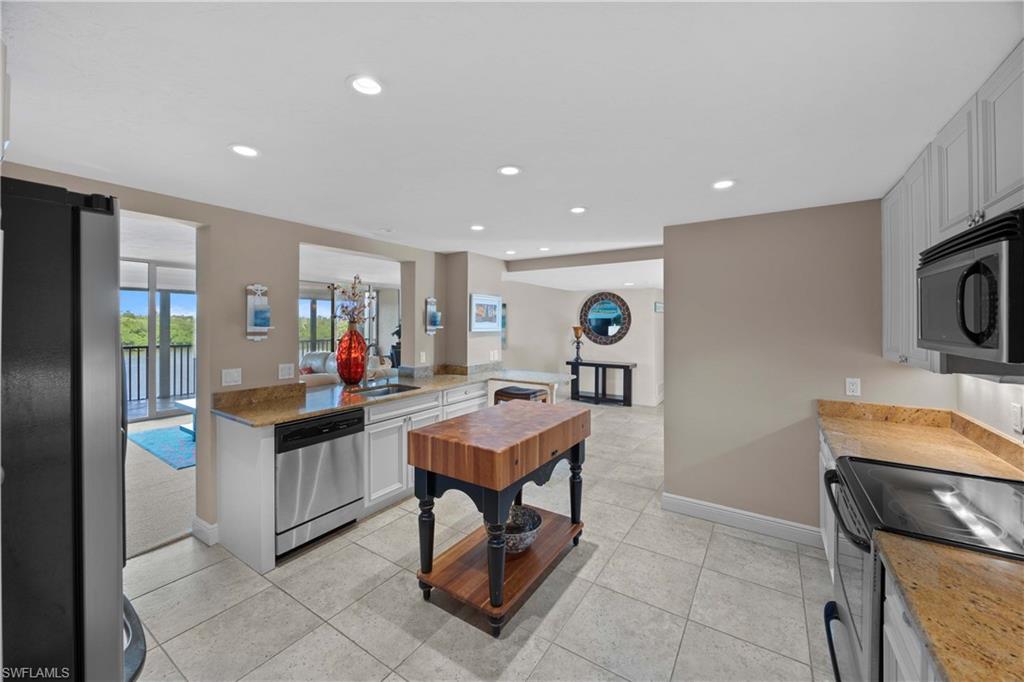 Kitchen with kitchen peninsula, appliances with stainless steel finishes, sink, white cabinetry, and light tile patterned flooring