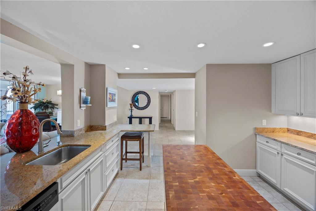 Kitchen featuring wooden counters, a breakfast bar, dishwashing machine, sink, and white cabinets