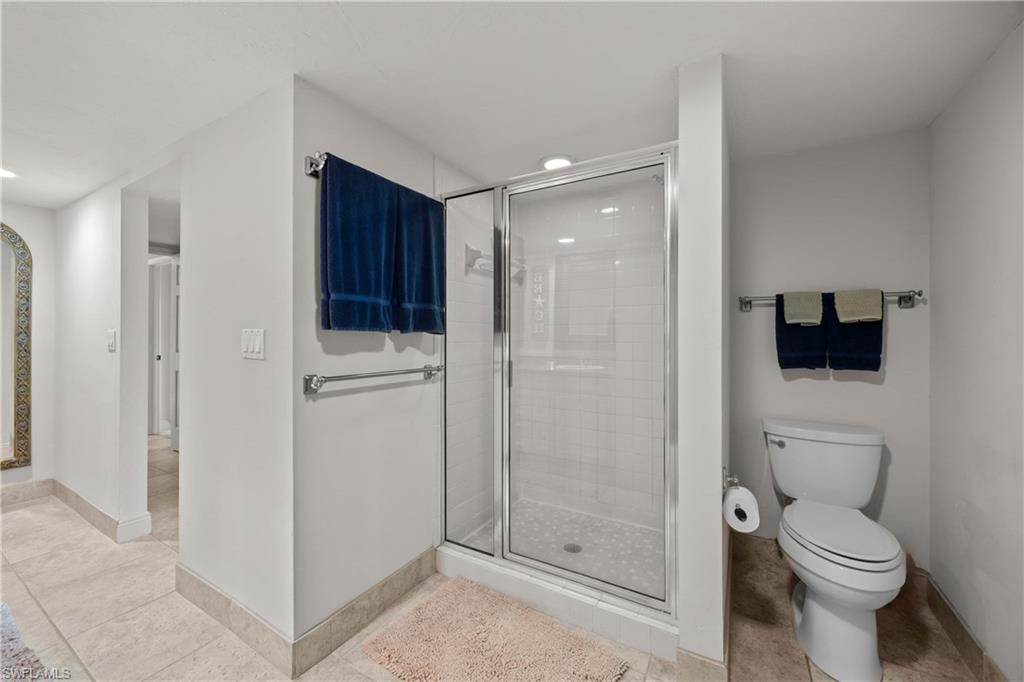 Bathroom with tile patterned floors, toilet, and a shower with door