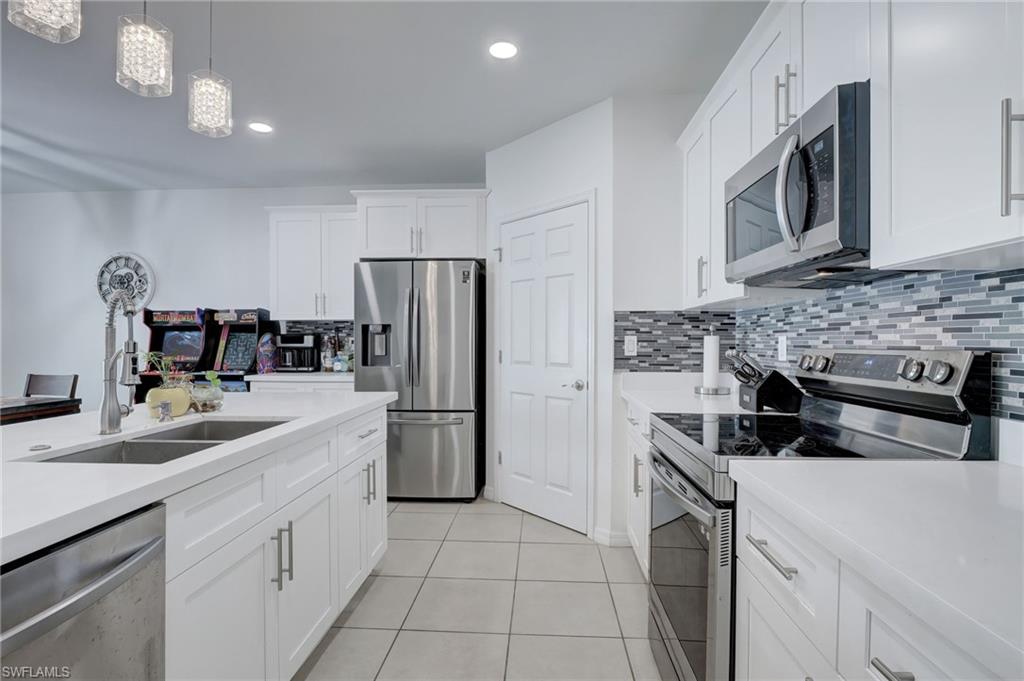 Kitchen featuring stainless steel appliances, white cabinets, backsplash, hanging light fixtures, and light tile patterned flooring