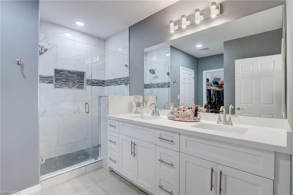 Full bathroom featuring a spacious closet, double vanity, a shower stall, and light tile patterned flooring