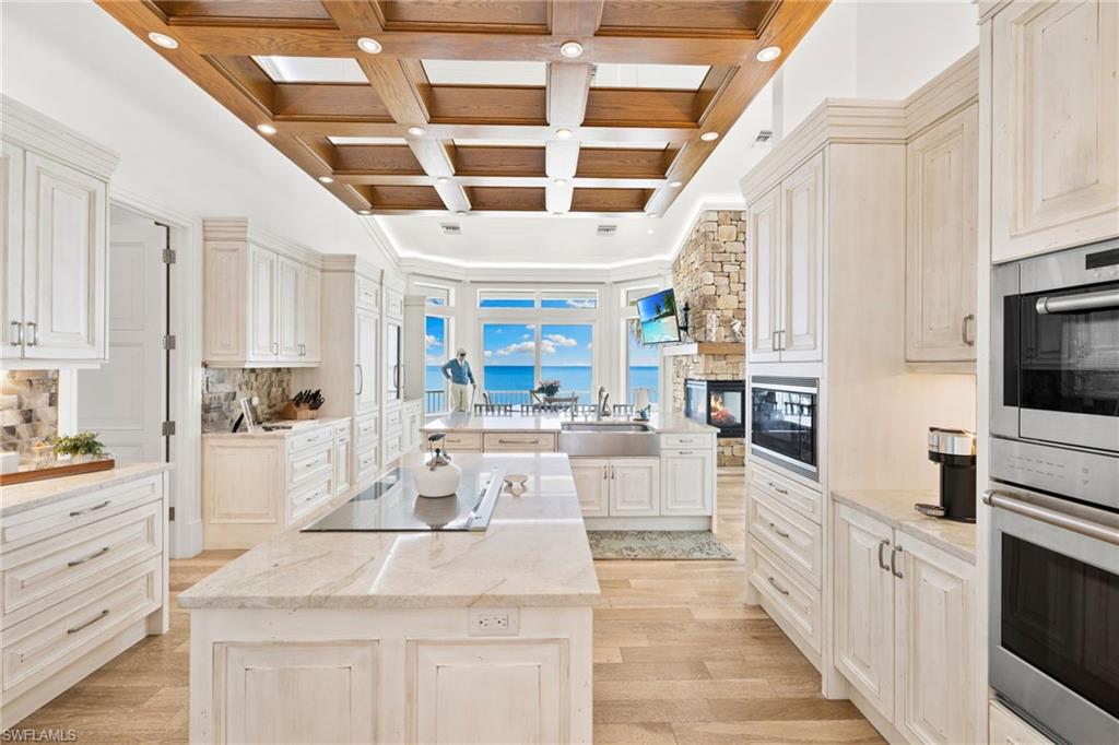 Kitchen featuring coffered ceiling, black appliances, a kitchen island, beamed ceiling, and light wood-style floors