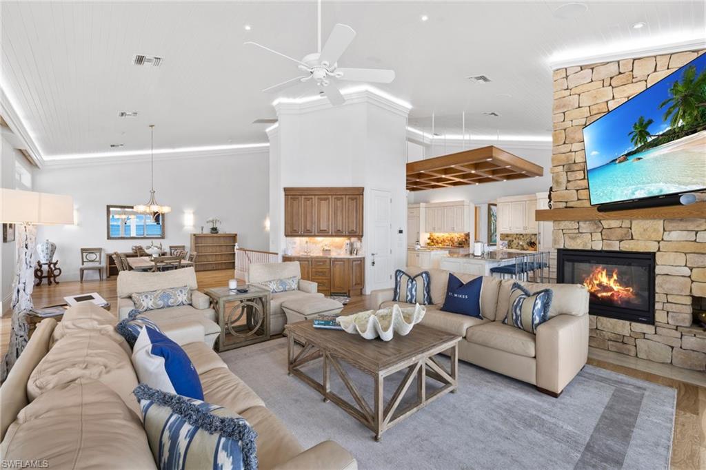 Living room with wood finished floors, crown molding, ceiling fan, a fireplace, and a chandelier