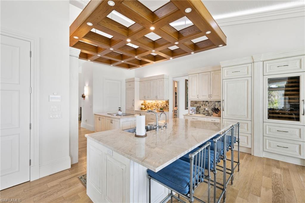Kitchen with coffered ceiling, a breakfast bar, backsplash, light wood-style flooring, and beam ceiling