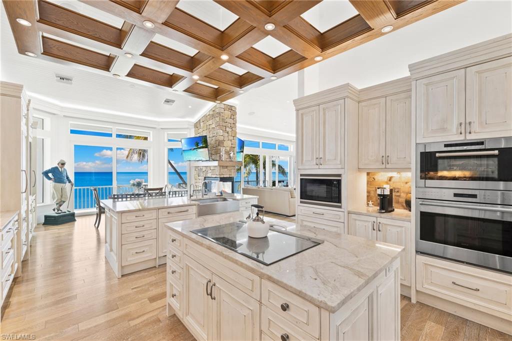 Kitchen with coffered ceiling, light stone countertops, black appliances, beamed ceiling, and light wood-type flooring