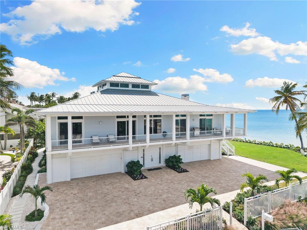 Raised beach house featuring a water view, a standing seam roof, a fenced front yard, a garage, and decorative driveway