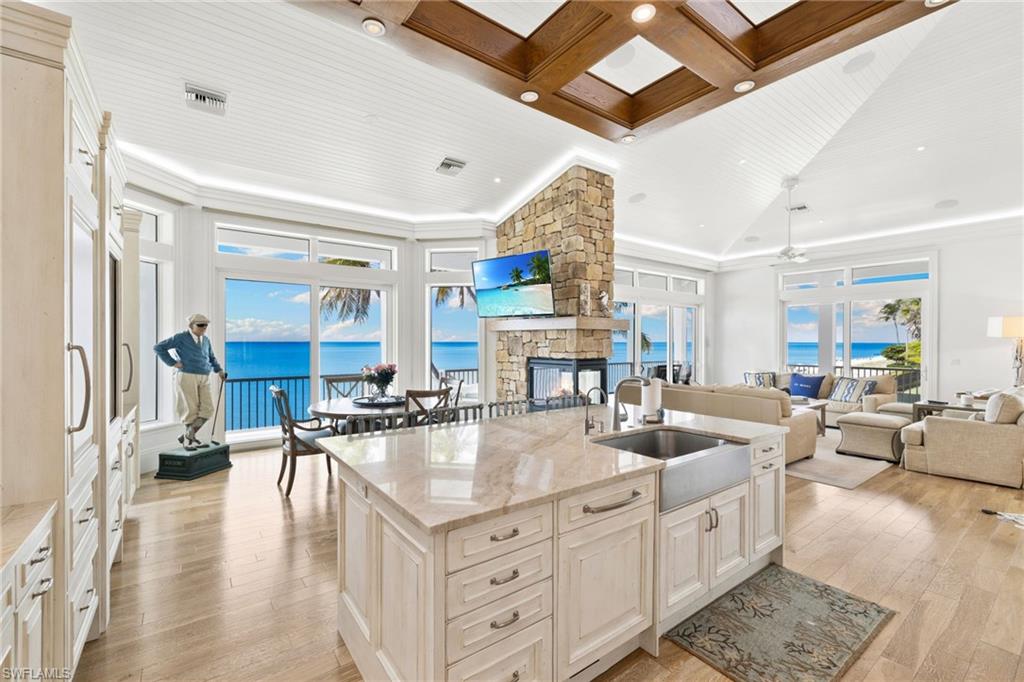 Kitchen featuring light stone countertops, coffered ceiling, open floor plan, a stone fireplace, and beamed ceiling