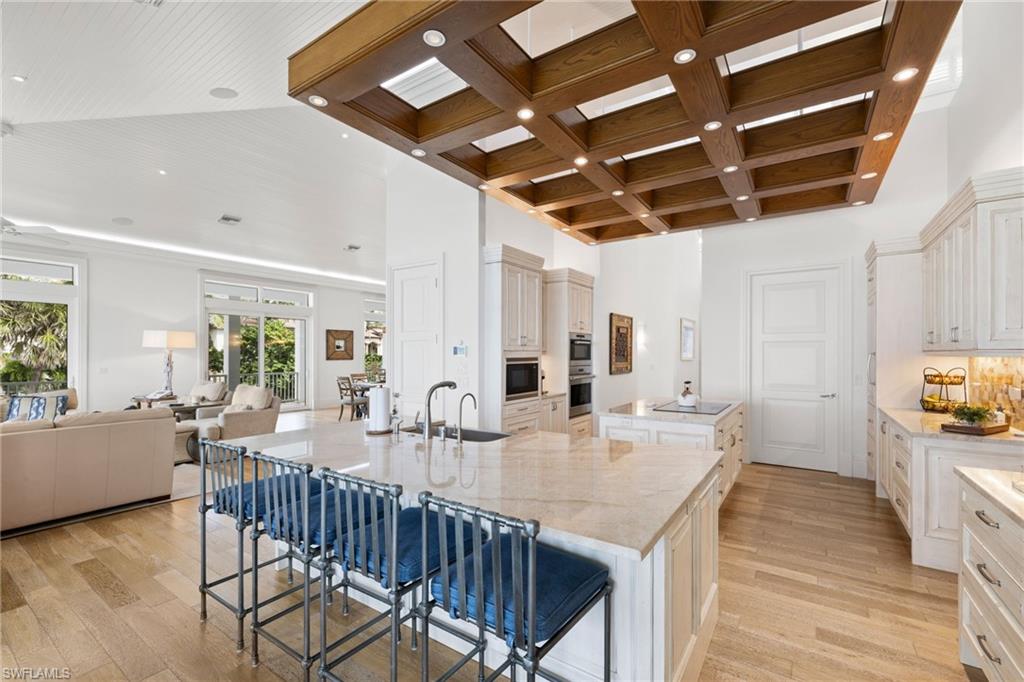 Kitchen featuring light wood-type flooring, a kitchen breakfast bar, open floor plan, light stone counters, and coffered ceiling