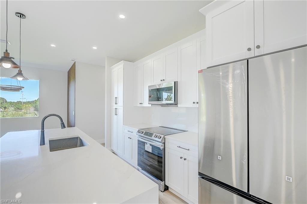 Kitchen featuring appliances with stainless steel finishes, a center island with sink, light stone countertops, white cabinets, and pendant lighting