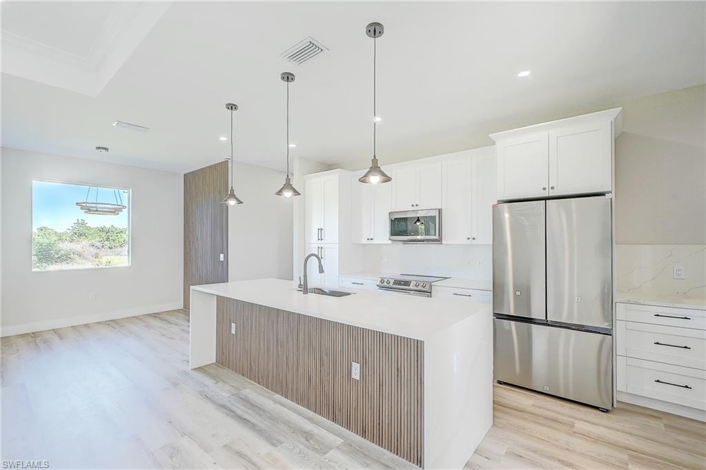 Kitchen with stainless steel appliances, white cabinetry, an island with sink, hanging light fixtures, and a kitchen breakfast bar