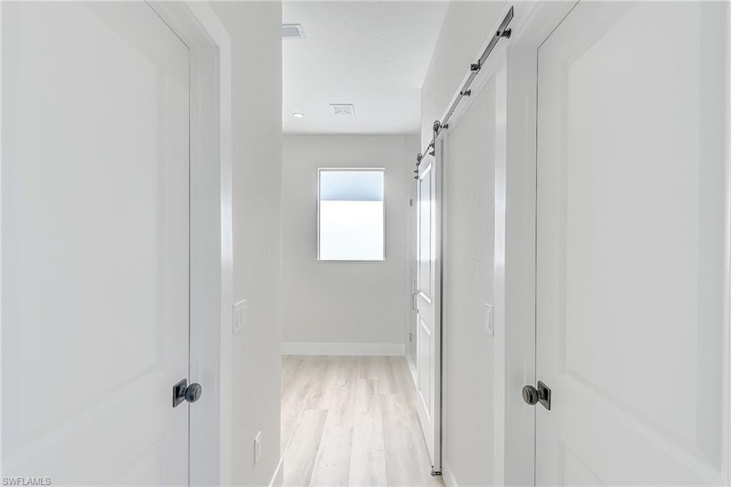 Bedroom featuring light wood-style floors, a raised ceiling, a ceiling fan, a barn door, and recessed lighting