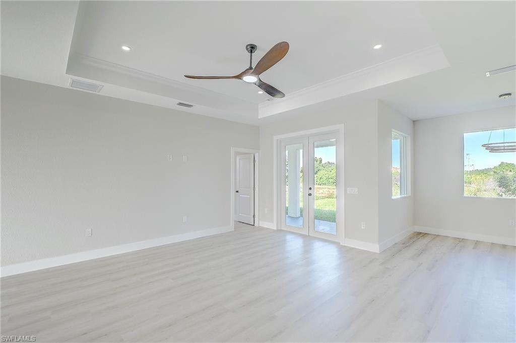 Kitchen with a raised ceiling, a kitchen bar, decorative light fixtures, light wood-style flooring, and white cabinets