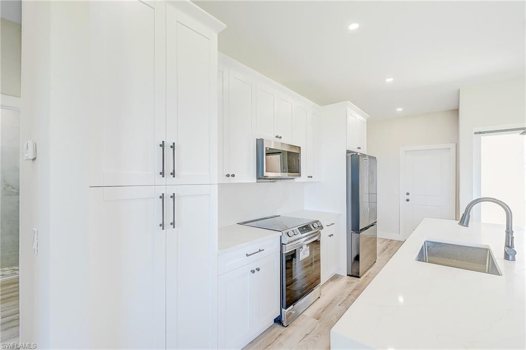 Kitchen featuring stainless steel appliances, hanging light fixtures, white cabinets, recessed lighting, and light stone counters