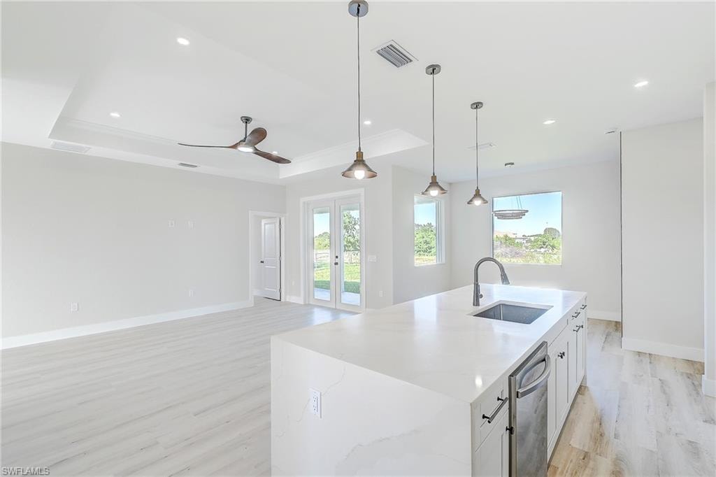 Kitchen featuring a raised ceiling, decorative light fixtures, light wood-style flooring, a center island with sink, and light stone countertops