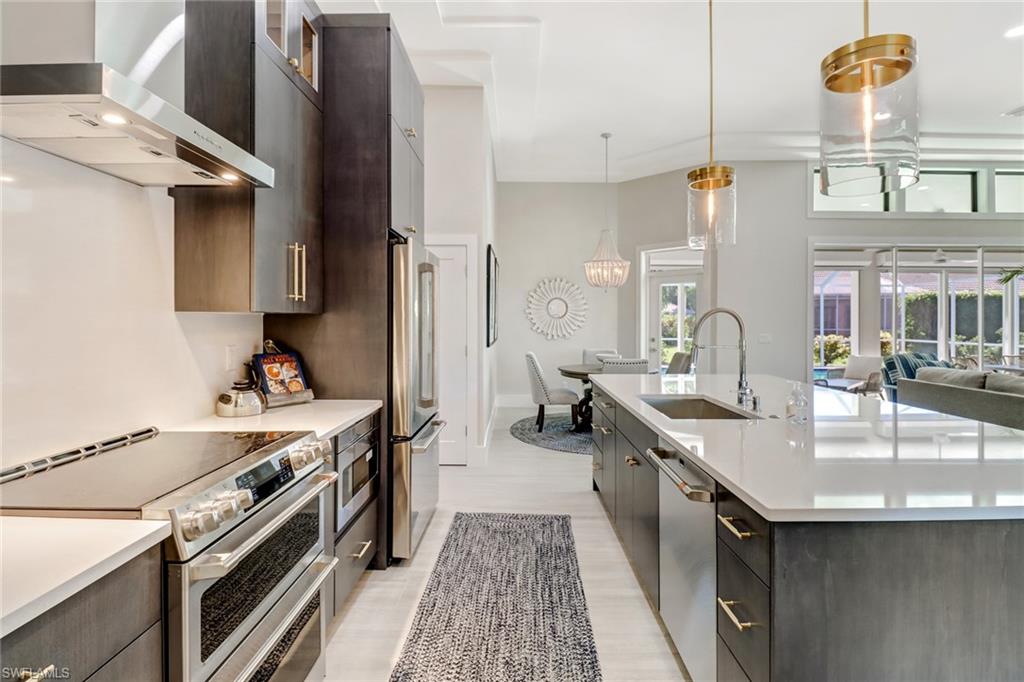 Kitchen featuring wall chimney range hood, appliances with stainless steel finishes, pendant lighting, glass insert cabinets, and open floor plan